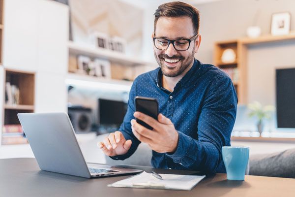 Mann sitzt mit PC und Smartphone am Tisch